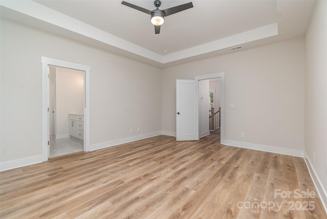 unfurnished bedroom with ceiling fan, light hardwood / wood-style flooring, a raised ceiling, and ensuite bath