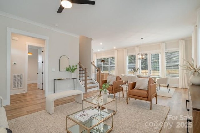 living room with ceiling fan with notable chandelier, ornamental molding, and light hardwood / wood-style flooring