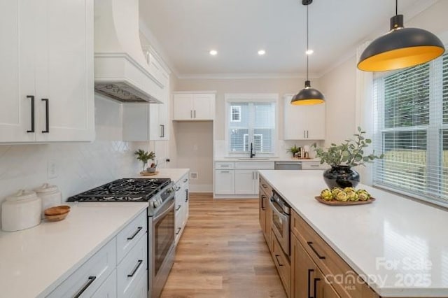 kitchen featuring stainless steel appliances, custom exhaust hood, white cabinets, and hanging light fixtures