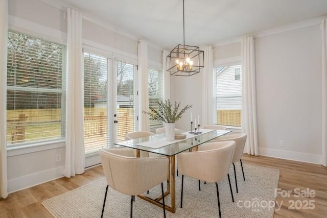 dining space featuring light wood-type flooring, crown molding, a healthy amount of sunlight, and a notable chandelier