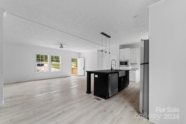 kitchen featuring a kitchen island with sink, white cabinets, decorative light fixtures, appliances with stainless steel finishes, and a textured ceiling