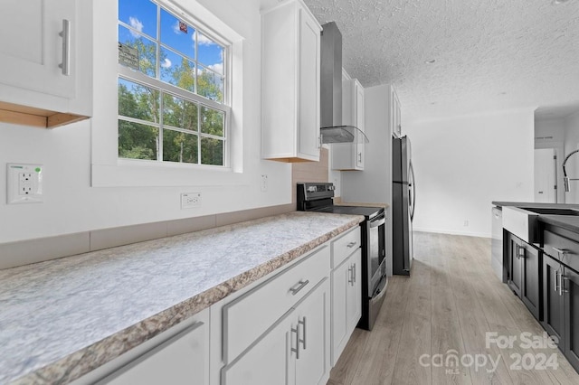 kitchen featuring wall chimney range hood, white cabinetry, light hardwood / wood-style flooring, sink, and stainless steel appliances