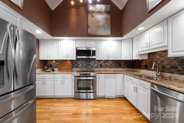 kitchen with stainless steel appliances, dark stone countertops, sink, white cabinetry, and light hardwood / wood-style floors