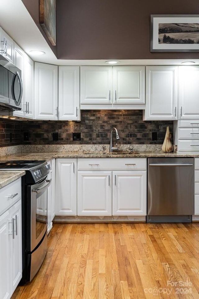 kitchen with white cabinetry, stone countertops, stainless steel appliances, and light wood-type flooring