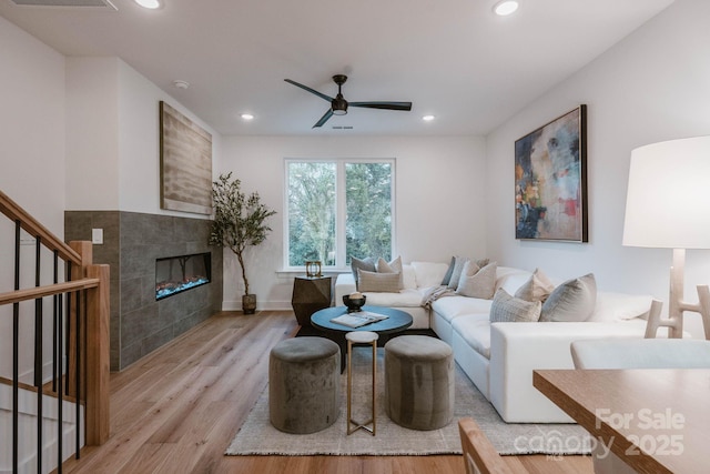 living room with ceiling fan, light wood-type flooring, and a tiled fireplace