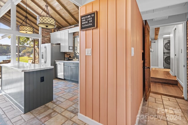 kitchen with dishwasher, vaulted ceiling with beams, stacked washer and clothes dryer, hanging light fixtures, and wooden ceiling