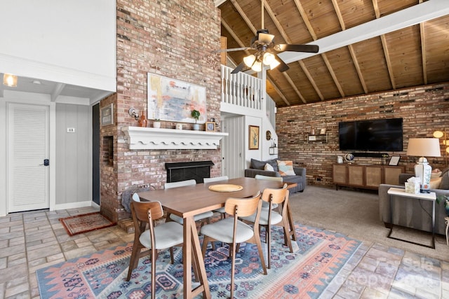 dining space with beam ceiling, ceiling fan, high vaulted ceiling, wooden ceiling, and a brick fireplace