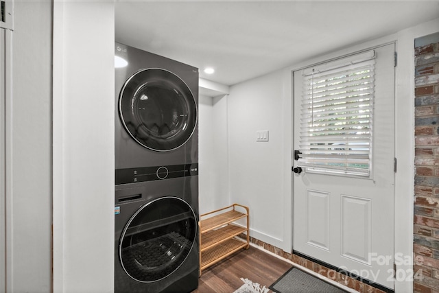 laundry area featuring stacked washer / dryer, brick wall, and dark hardwood / wood-style flooring