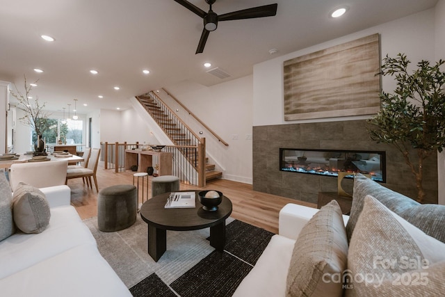 living room with light wood-type flooring, ceiling fan, and a tile fireplace