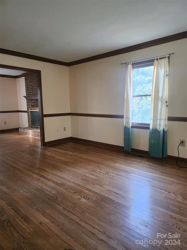 spare room with crown molding, a brick fireplace, and dark hardwood / wood-style floors