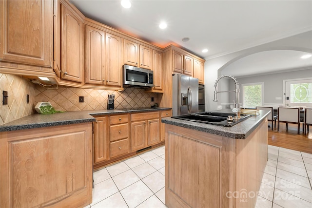 kitchen with light tile patterned flooring, sink, stainless steel appliances, a kitchen island with sink, and decorative backsplash