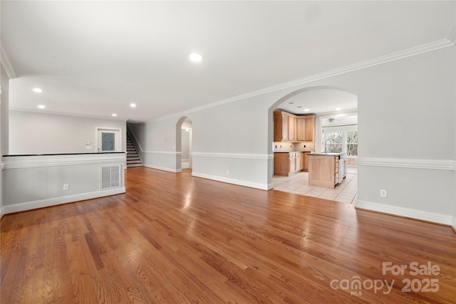 unfurnished living room featuring crown molding, sink, and light hardwood / wood-style floors