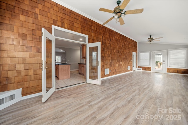 unfurnished living room featuring lofted ceiling, ceiling fan, wooden walls, ornamental molding, and light wood-type flooring