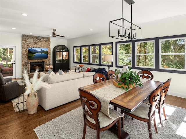 dining room with dark wood-type flooring, ornamental molding, a fireplace, and ceiling fan with notable chandelier