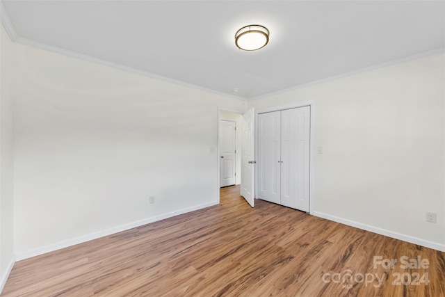 unfurnished bedroom with a closet, crown molding, and light wood-type flooring