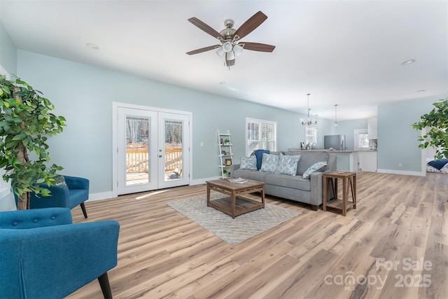 living area featuring french doors, baseboards, light wood finished floors, and ceiling fan with notable chandelier