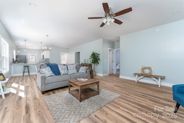 living room with ceiling fan with notable chandelier, light wood-type flooring, and baseboards