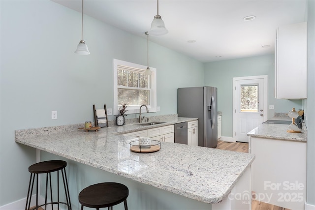 kitchen with a breakfast bar, appliances with stainless steel finishes, white cabinets, a sink, and a peninsula