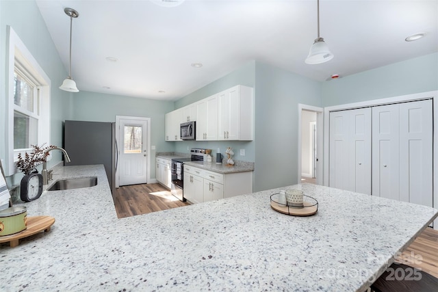 kitchen featuring light stone counters, stainless steel appliances, a sink, wood finished floors, and white cabinets