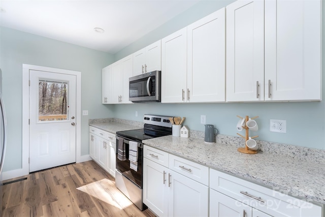 kitchen with light stone countertops, light wood-style floors, white cabinetry, and appliances with stainless steel finishes