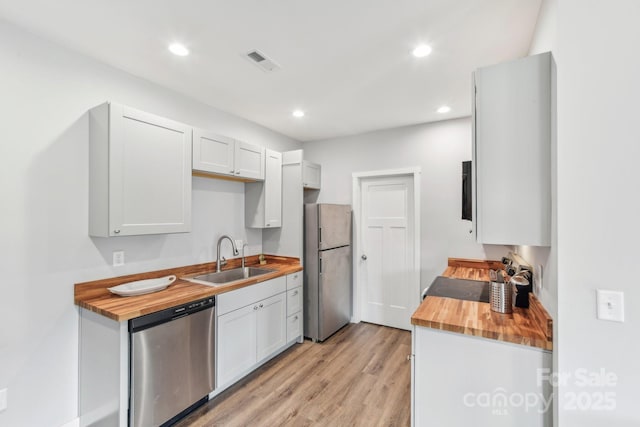 kitchen with light wood finished floors, visible vents, butcher block countertops, stainless steel appliances, and a sink