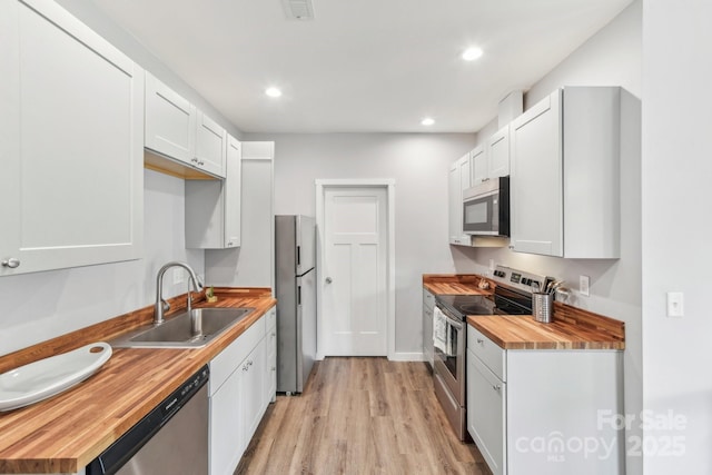 kitchen with stainless steel appliances, recessed lighting, wooden counters, light wood-style flooring, and a sink