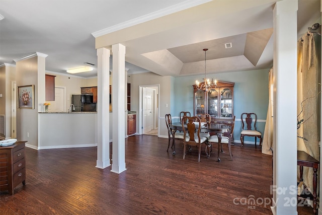 dining space featuring a raised ceiling, dark hardwood / wood-style flooring, ornate columns, a notable chandelier, and ornamental molding