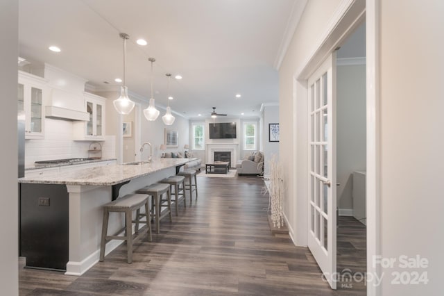 kitchen with dark hardwood / wood-style flooring, pendant lighting, an island with sink, backsplash, and white cabinetry