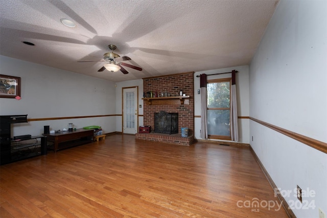 living room with a brick fireplace, light hardwood / wood-style flooring, and a textured ceiling