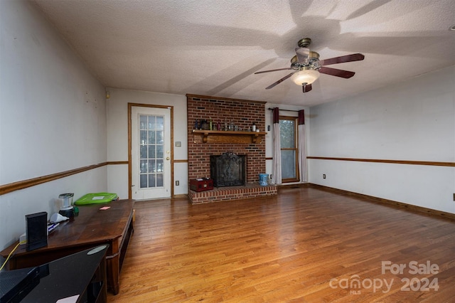 living room with light wood-type flooring, a textured ceiling, ceiling fan, and a fireplace