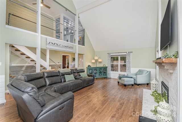 living room featuring wood-type flooring, beam ceiling, high vaulted ceiling, a brick fireplace, and ceiling fan