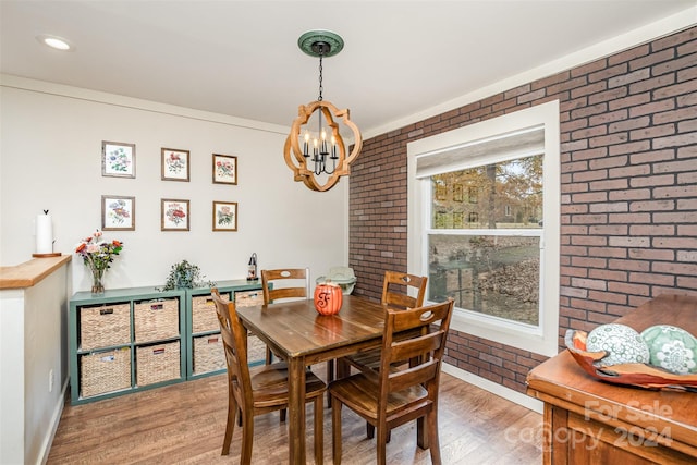 dining room with hardwood / wood-style floors, brick wall, crown molding, and a notable chandelier