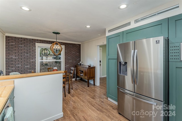 kitchen with light wood-type flooring, stainless steel fridge with ice dispenser, green cabinets, hanging light fixtures, and brick wall