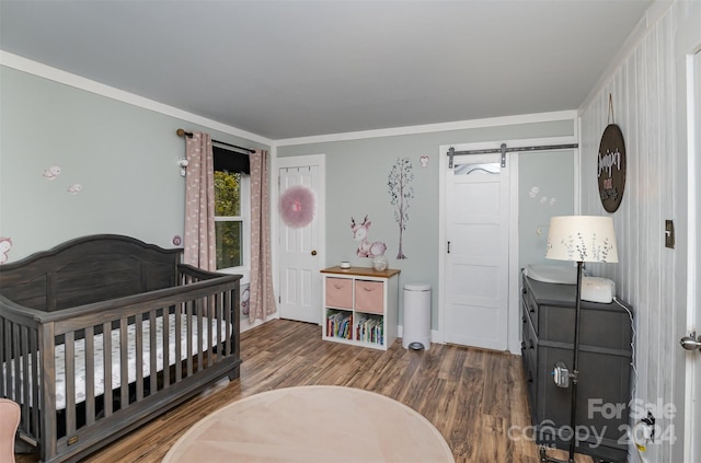 bedroom featuring ornamental molding, a nursery area, a barn door, and dark hardwood / wood-style floors