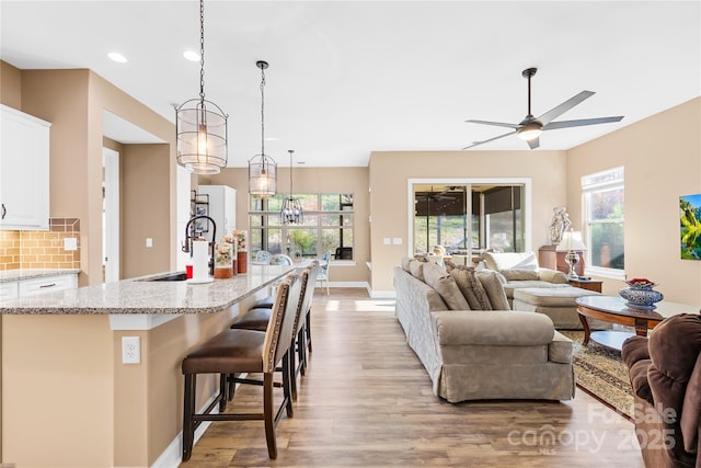 living room featuring ceiling fan with notable chandelier, light hardwood / wood-style floors, a healthy amount of sunlight, and sink