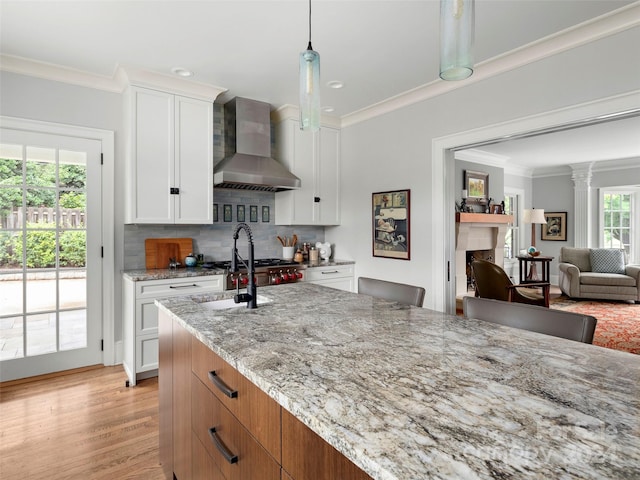 kitchen with wall chimney range hood, light hardwood / wood-style flooring, crown molding, light stone countertops, and white cabinets