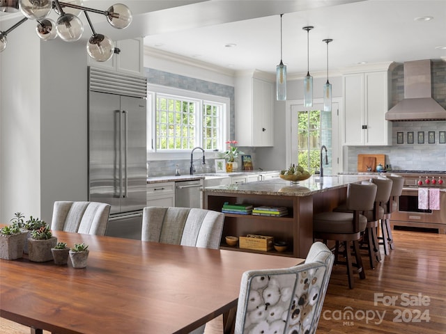 kitchen featuring wall chimney exhaust hood, dark wood-type flooring, premium appliances, white cabinets, and light stone counters