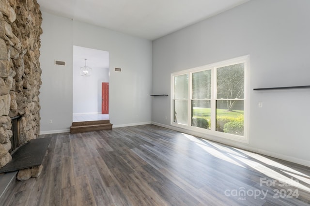 unfurnished living room featuring a stone fireplace, hardwood / wood-style floors, and a chandelier