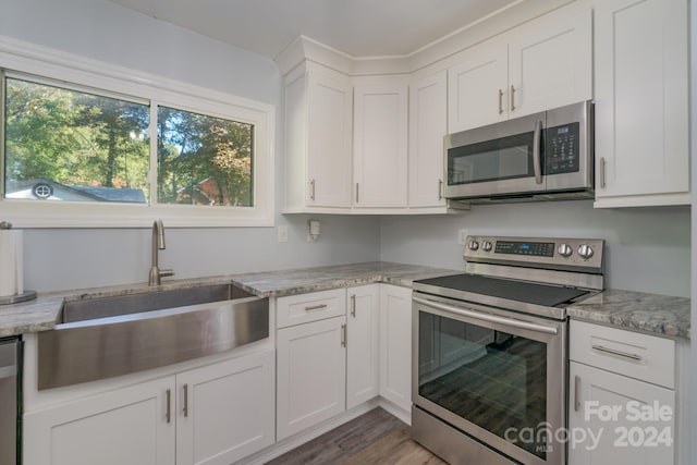 kitchen with dark wood-type flooring, stainless steel appliances, sink, light stone countertops, and white cabinetry