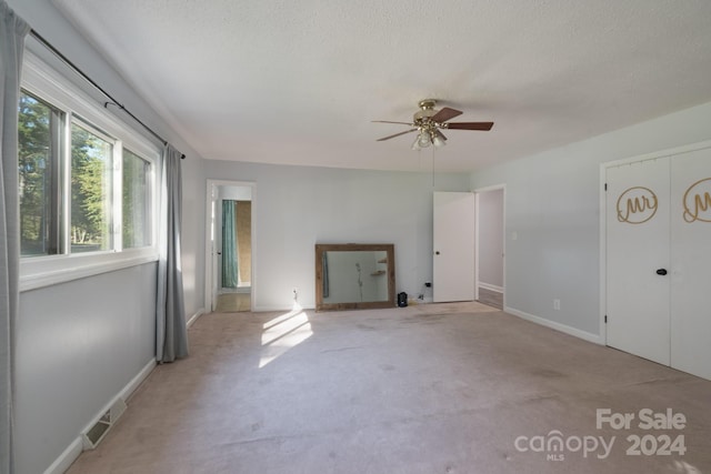 empty room with a textured ceiling, light colored carpet, and ceiling fan