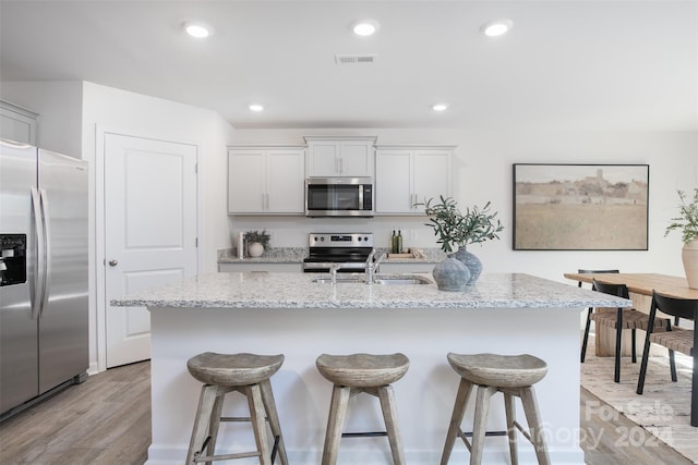 kitchen with white cabinets, stainless steel appliances, a center island with sink, and light wood-type flooring