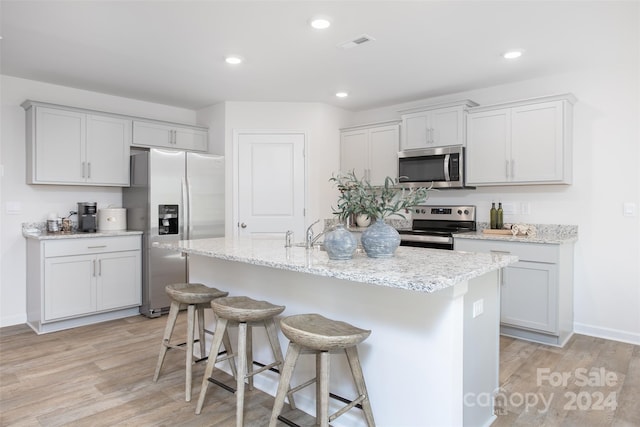 kitchen featuring light hardwood / wood-style flooring, light stone countertops, stainless steel appliances, a breakfast bar, and a center island with sink