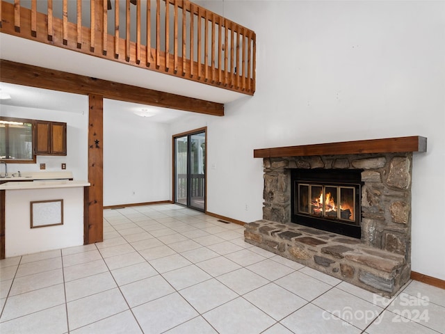 unfurnished living room featuring a stone fireplace, beam ceiling, light tile patterned flooring, and sink