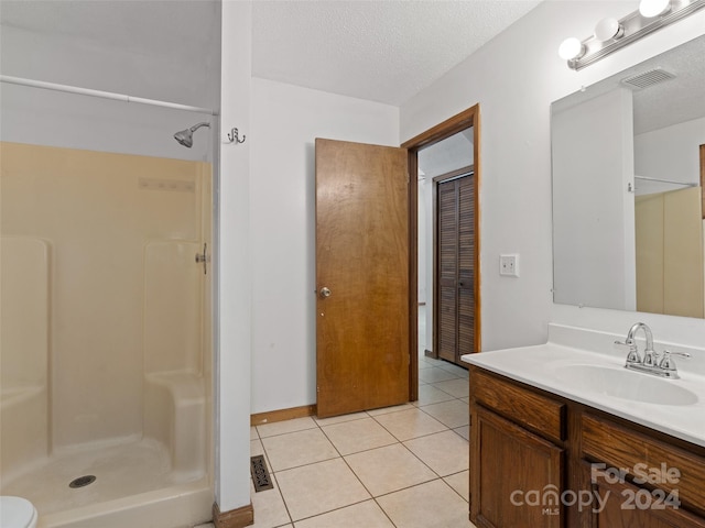 bathroom featuring vanity, a textured ceiling, walk in shower, and tile patterned flooring