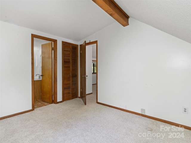 unfurnished bedroom with light carpet, vaulted ceiling with beams, and a textured ceiling