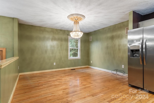 unfurnished dining area with light wood-type flooring, a notable chandelier, and a textured ceiling