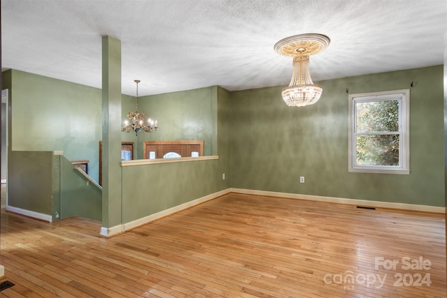 empty room with a textured ceiling, a notable chandelier, and light hardwood / wood-style flooring