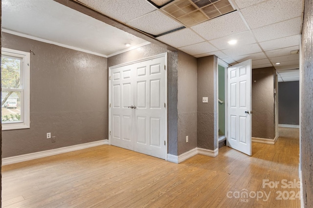 unfurnished bedroom with a paneled ceiling, a closet, and light hardwood / wood-style flooring