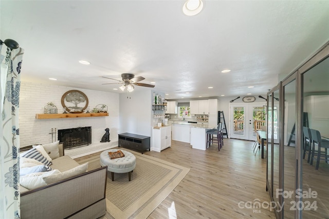 living room featuring light hardwood / wood-style flooring, ceiling fan, and a brick fireplace