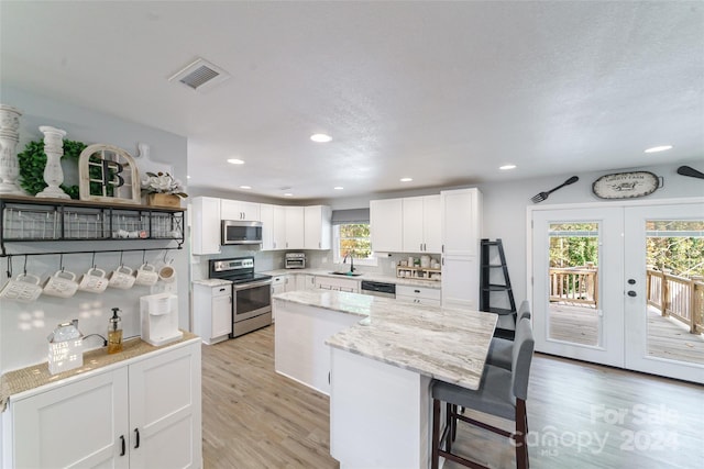 kitchen featuring a kitchen island, stainless steel appliances, sink, light wood-type flooring, and white cabinetry